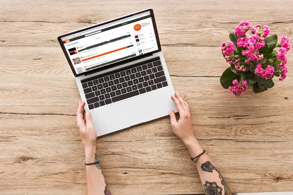 Vue partielle de la femme sur la table avec ordinateur portable avec logo soundcloud et plante kalanhoe en pot de fleurs — Photo de stock