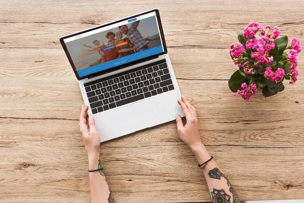 Partial view of woman at tabletop with laptop with couchsurfing website and kalanhoe plant in flowerpot — Stock Photo