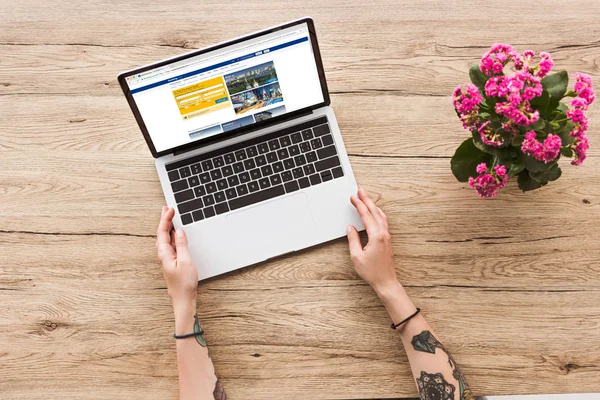 Visão parcial da mulher na mesa com laptop com logotipo bookingcom e planta kalanhoe em vaso de flores — Fotografia de Stock