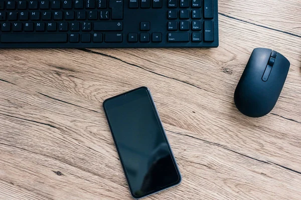 Закрытый вид смартфона с экраном, компьютерной клавиатурой и компьютерной мышью на деревянном столе — стоковое фото