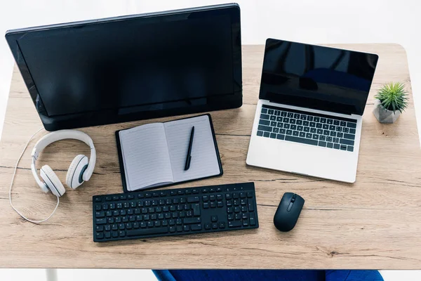 Повышенный вид стола с ноутбуком, компьютером, пустым учебником, ручкой и наушниками — стоковое фото
