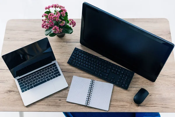 Vista elevada de la mesa con flores, libro de texto vacío, computadora portátil y computadora con pantallas en blanco — Stock Photo