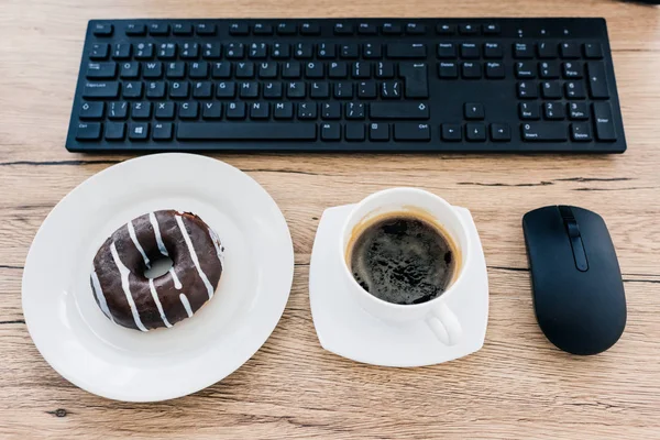 Draufsicht auf Donut, Kaffeetasse, Computermaus und Computertastatur auf Holztisch — Stockfoto