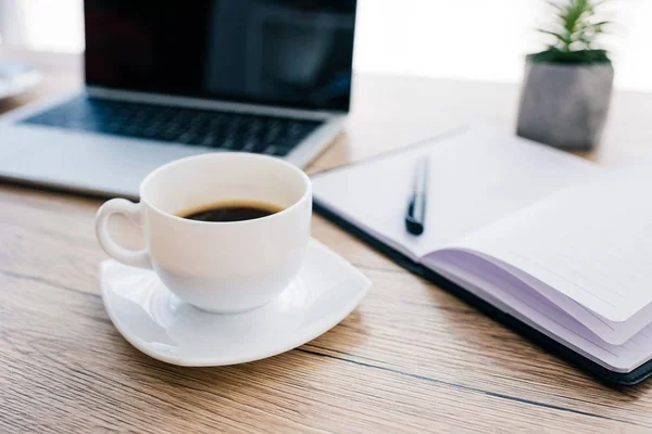 Close up view of coffee cup, empty textbook and laptop with blank screen on wooden table — Stock Photo