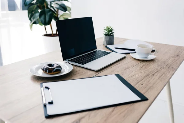 Vista close-up de área de transferência vazia, donut, xícara de café, planta envasada, livro didático e laptop na mesa de madeira — Fotografia de Stock