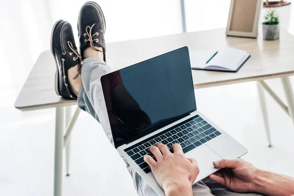 Teilbild eines Mannes, der Beine auf dem Tisch hält und auf dem Laptop tippt — Stockfoto