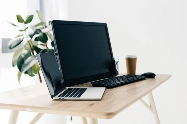 Vista frontal do local de trabalho com laptop, computador, xícara de papel de café na mesa e vaso planta — Fotografia de Stock