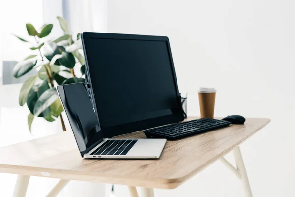 Front view of workplace with laptop, computer, paper cup of coffee on table and potted plant — Stock Photo