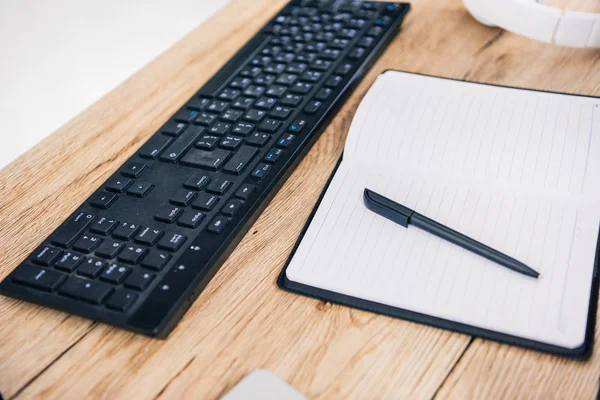 Closeup shot of computer keyboard, empty textbook with pen and headphones at table — Stock Photo