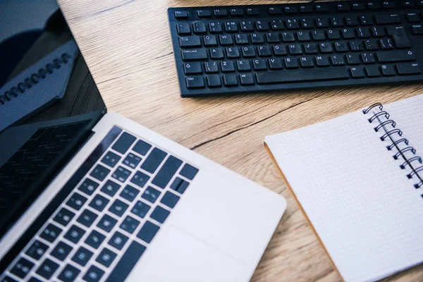 Ansicht des Laptops mit leerem Bildschirm, leerem Lehrbuch und Computertastatur am Tisch — Stockfoto