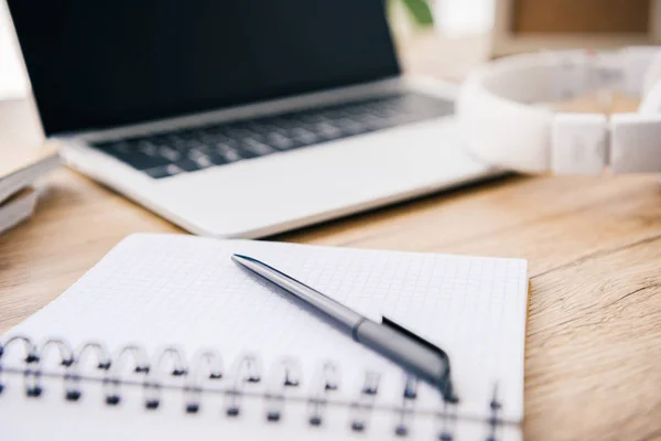 Nahaufnahme eines leeren Lehrbuchs mit Stift am Tisch mit Laptop und Kopfhörer — Stockfoto