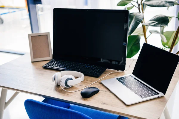 Vista close-up do local de trabalho com laptop, fones de ouvido, moldura de foto e computador à mesa — Fotografia de Stock