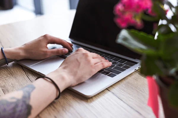 Cropped image of woman with tattooed hands typing on laptop at table with flowers — Stock Photo