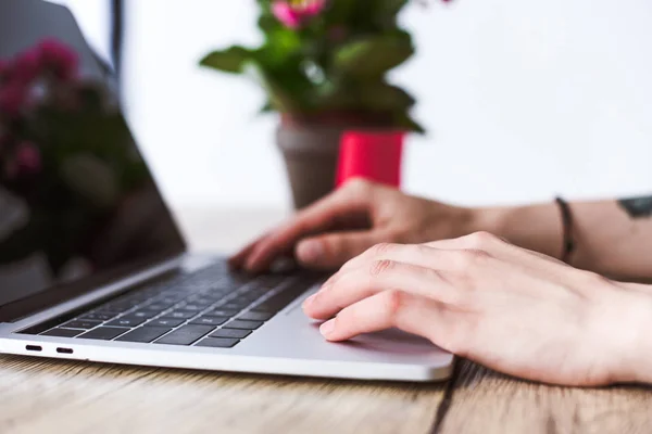 Cropped shot of woman typing on laptop with blank screen at table with flowers — Stock Photo