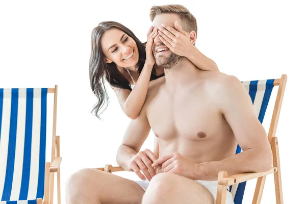 Menina feliz fechar os olhos de seu namorado e fazer surpresa em cadeiras de praia, isolado no branco — Fotografia de Stock