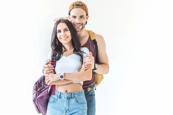 Couple of tourists with backpacks hugging and looking at camera, isolated on white — Stock Photo