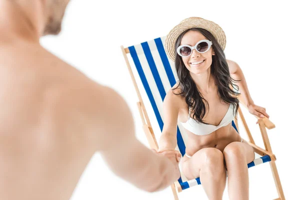 Hermosa mujer alegre en traje de baño y gafas de sol tomando las manos de su novio, aislado en blanco - foto de stock