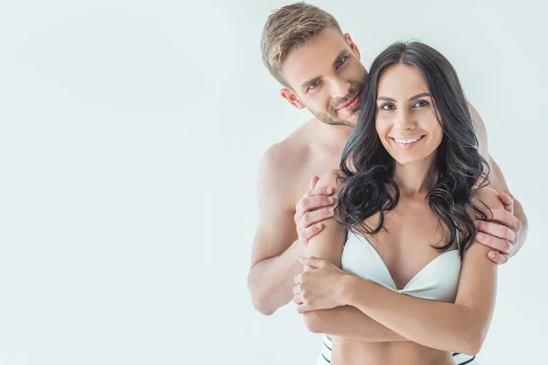 Bel homme étreignant sa petite amie souriante en maillot de bain, isolé sur blanc — Photo de stock