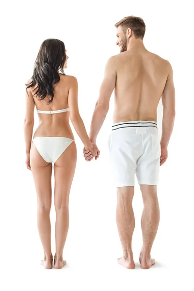 Вид сзади молодой веселой пары в купальниках, держащихся за руки, изолированных на белом — стоковое фото