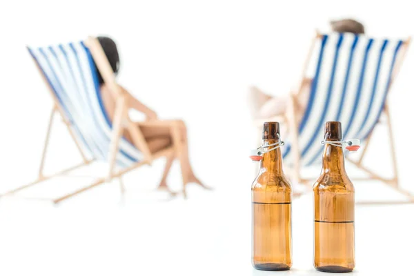 Selective focus of couple resting on beach chairs, with bottles of beer on foreground, isolated on white — Stock Photo