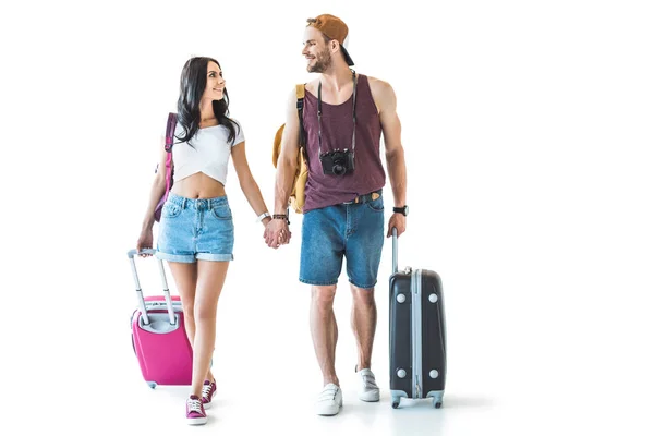 Young travelers with travel bags holding hands and looking at each other, isolated on white — Stock Photo