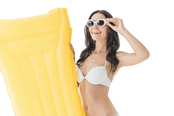 Hermosa mujer sonriente en bikini y gafas de sol sosteniendo colchón inflable amarillo, aislado en blanco - foto de stock
