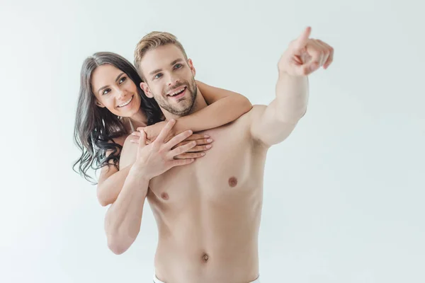 Beautiful young woman hugging boyfriend pointing somewhere, isolated on white — Stock Photo