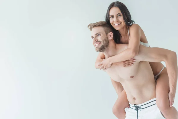 Hermosa feliz pareja en traje de baño piggybacking aislado en blanco - foto de stock