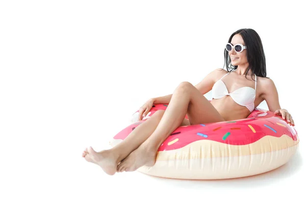 Beautiful girl in bikini and sunglasses lying on inflatable donut, isolated on white — Stock Photo