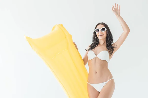 Femme heureuse en bikini et lunettes de soleil agitant et tenant matelas gonflable, isolé sur blanc — Photo de stock