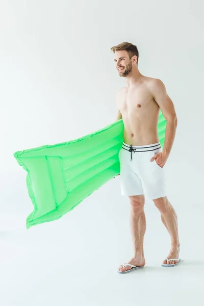 Усміхнений чоловік у купальнику з зеленим надувним матрацом, ізольований на білому — стокове фото