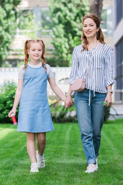 Sonrientes madre e hija con pompas de jabón cogidas de la mano - foto de stock