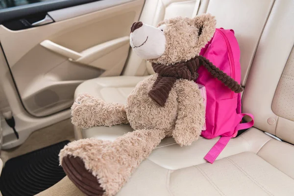 Vista de cerca del oso de peluche con mochila rosa en el asiento en el coche - foto de stock