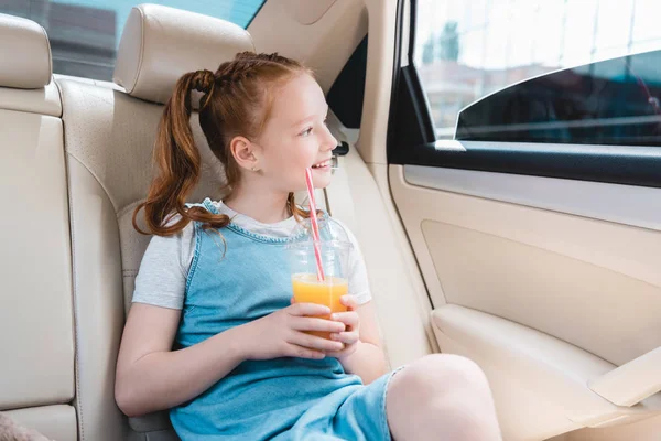 Enfant gai avec du jus regardant par la fenêtre de la voiture tout en étant assis dans la voiture — Photo de stock