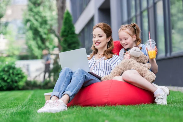 Mother and daughter using laptop while resting on bag chair together — Stock Photo