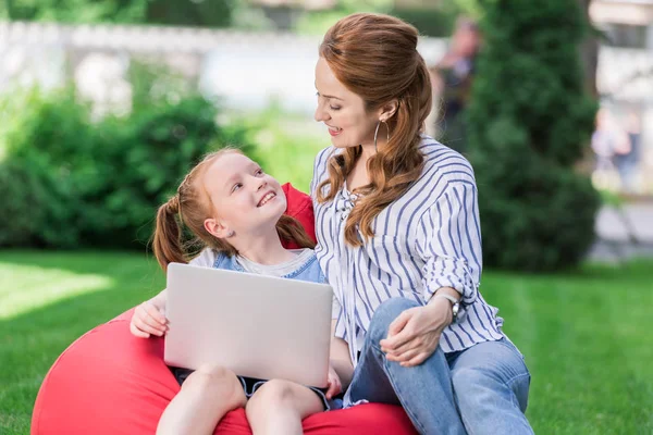 Smiling mother and daughter with laptop resting on bag chair together — Stock Photo