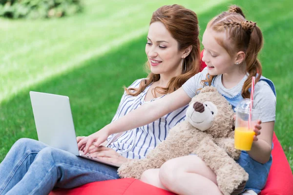 Усміхнена мати і дочка використовують ноутбук, відпочиваючи на мішках разом — стокове фото