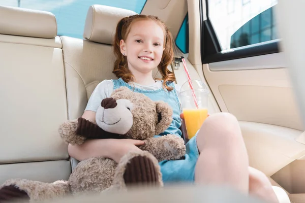 Portrait of smiling child with juice and teddy bear in car — Stock Photo