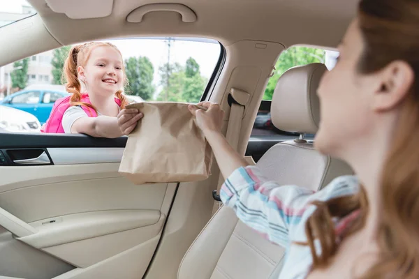 Teilbild einer Frau im Auto, die ihrer Tochter Papierpaket mit Lebensmitteln schenkt — Stockfoto