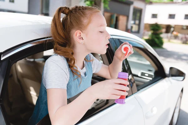 Vue latérale des bulles de savon de soufflage d'enfant tout en étant assis dans la voiture — Photo de stock