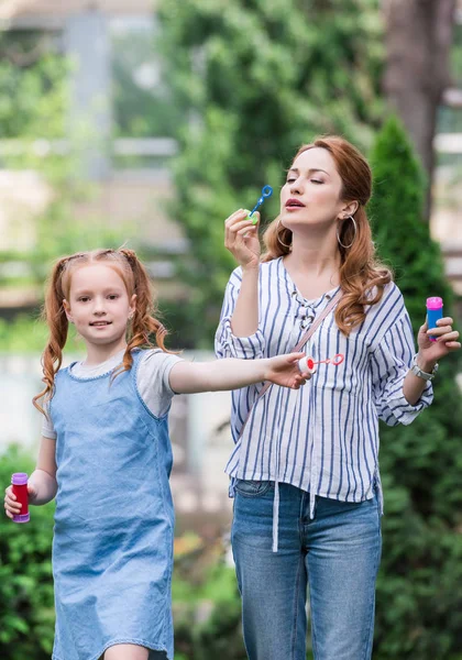 Portrait of mother and daughter blowing soap bubbles in park — Stock Photo