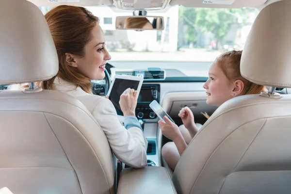 Vue arrière de la famille souriante avec des appareils numériques dans la voiture — Photo de stock
