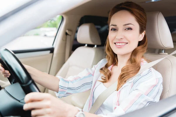 Side view of smiling woman looking at camera while driving car — Stock Photo