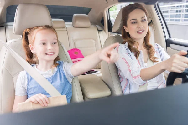 Портрет усміхненої жінки, яка керує автомобілем і дочкою, що вказує на пасажирське сидіння — стокове фото