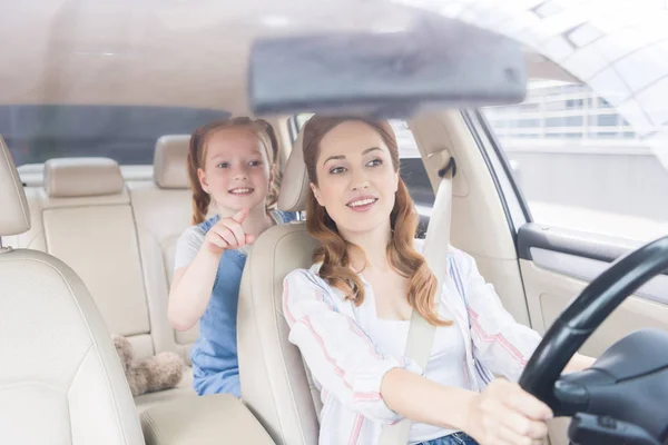 Retrato de mulher sorridente dirigindo carro e filha apontando para longe no assento dos passageiros — Fotografia de Stock
