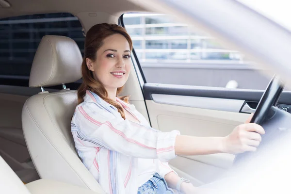 Vue latérale de la femme souriante regardant la caméra tout en conduisant la voiture — Photo de stock