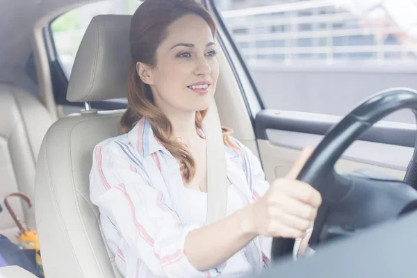 Retrato de la mujer sonriente con las manos en el volante de conducción del coche - foto de stock