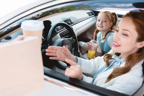 Enfoque selectivo de la mujer de negocios sonriente tomando orden de llevar con la hija en el asiento de pasajeros en el coche — Stock Photo