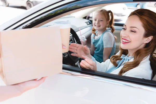 Selective focus of smiling businesswoman taking take away order with daughter on passengers seat in car — Stock Photo