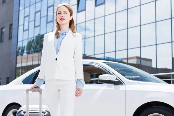 Ritratto di donna d'affari in abito bianco con valigia in piedi in auto sulla strada — Foto stock